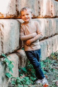 Young boy posing leaning against rock wall with Ron Schroll Photography at Bridge to Antiquity in Davidson, NC.