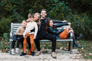 Family sitting on bench taking fall photos with Ron Schroll Photography at Bridge to Antiquity in Davidson, NC.